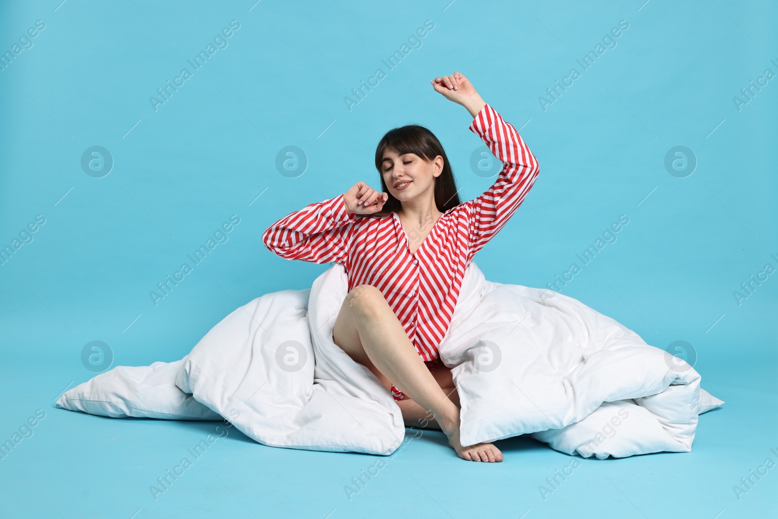 Photo of Happy woman with pyjama and blanket stretching on light blue background