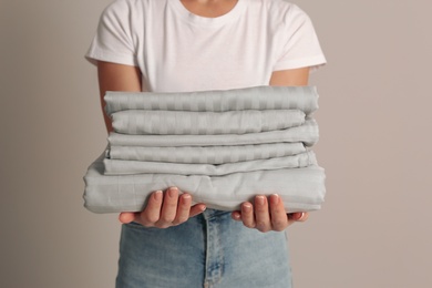 Photo of Woman holding stack of clean bed linens on beige background