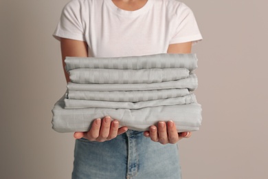 Woman holding stack of clean bed linens on beige background