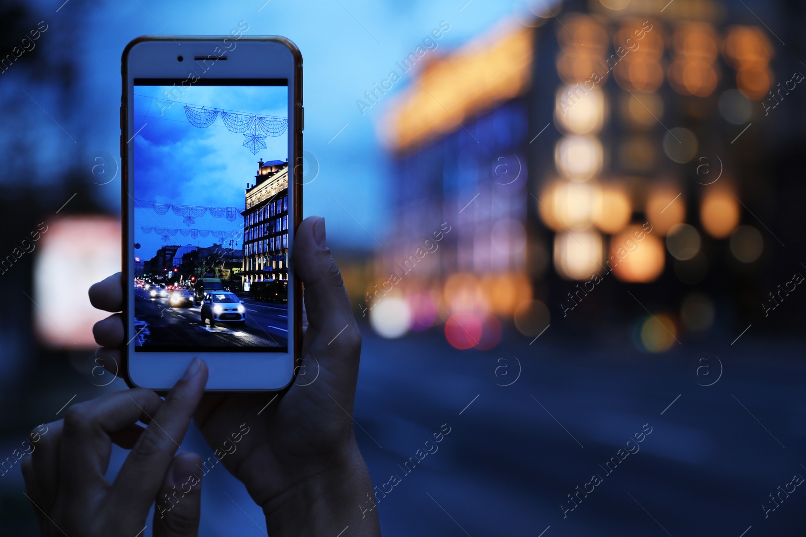 Photo of Woman taking photo of modern city in evening with smartphone, focus on hand. Bokeh effect