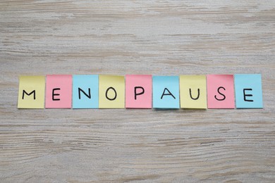Photo of Colorful paper notes with word Menopause on wooden table, flat lay