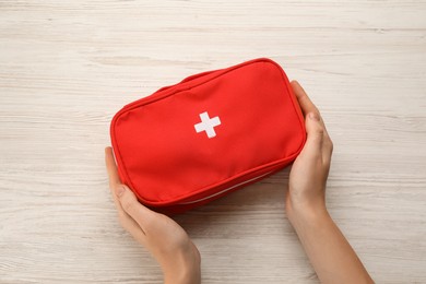 Woman holding first aid kit bag at white wooden table, top view