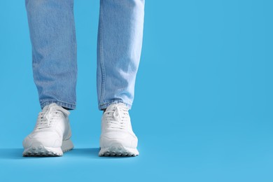 Man wearing stylish sneakers on light blue background, closeup. Space for text