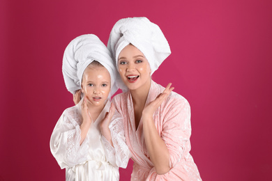 Emotional mother and daughter with facial masks on pink background
