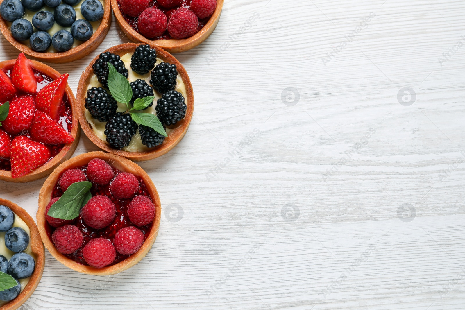 Photo of Tartlets with different fresh berries on white wooden table, flat lay and space for text. Delicious dessert