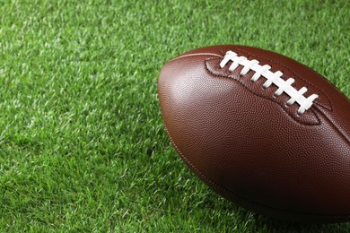 Photo of Leather American football ball on green grass, closeup. Space for text