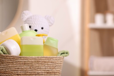 Photo of Baby cosmetic products, bath accessories and toy bear in wicker basket indoors, closeup. Space for text