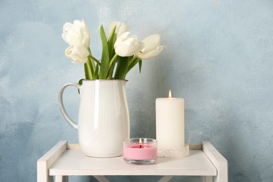 Photo of Beautiful white tulips and burning candles on wooden table against light blue background