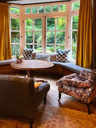 Photo of Wooden table near bay window seat with cushions in cozy room. Interior design