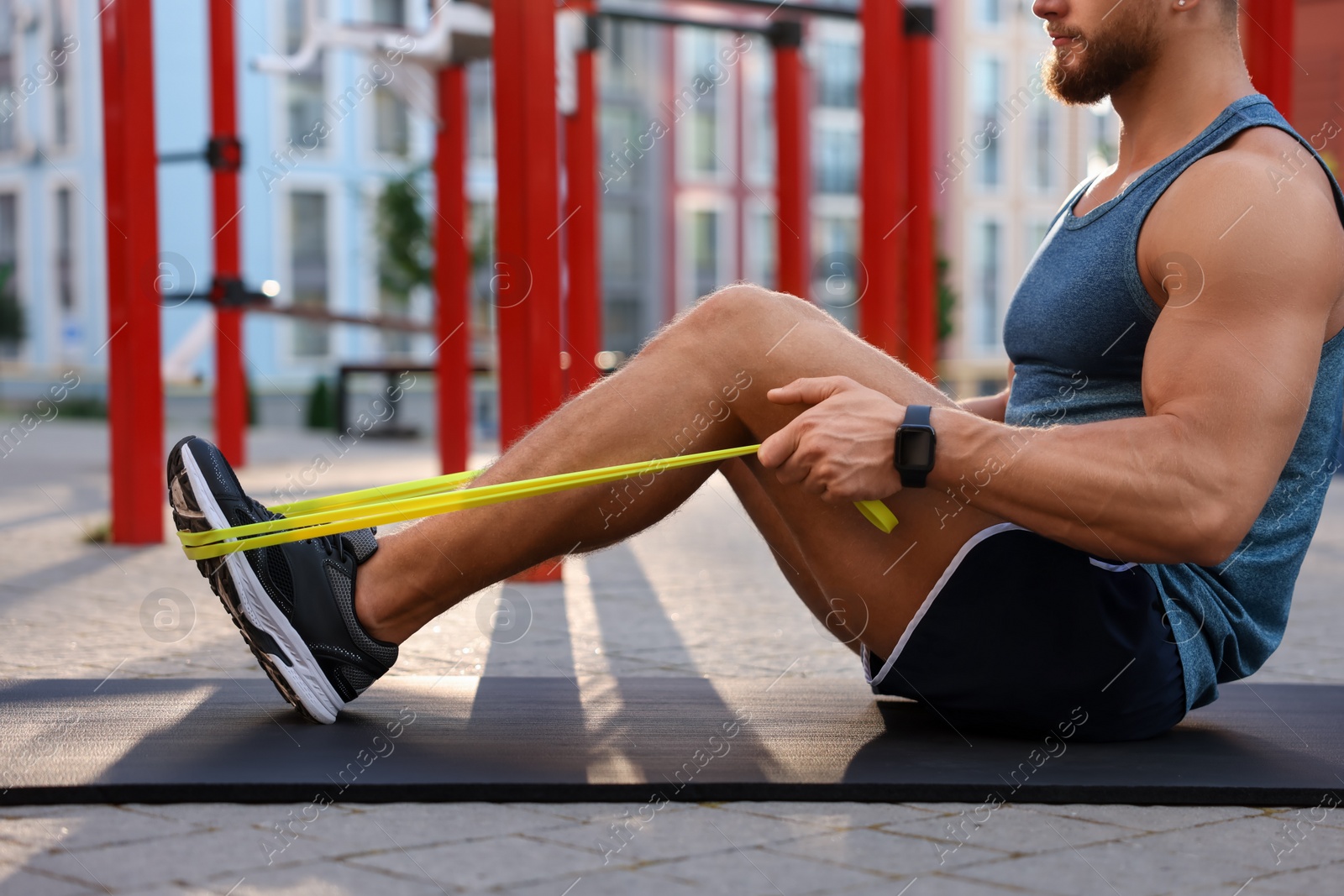 Photo of Muscular man doing exercise with elastic resistance band on mat at sports ground, closeup