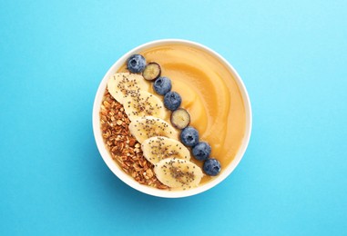 Photo of Delicious smoothie bowl with fresh blueberries, banana and granola on light blue background, top view