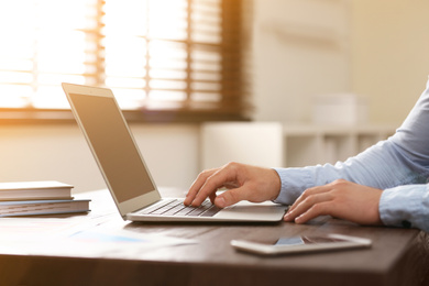 Man working with laptop at table in office, closeup