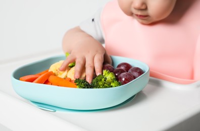Photo of Cute little baby wearing bib while eating on white background, closeup