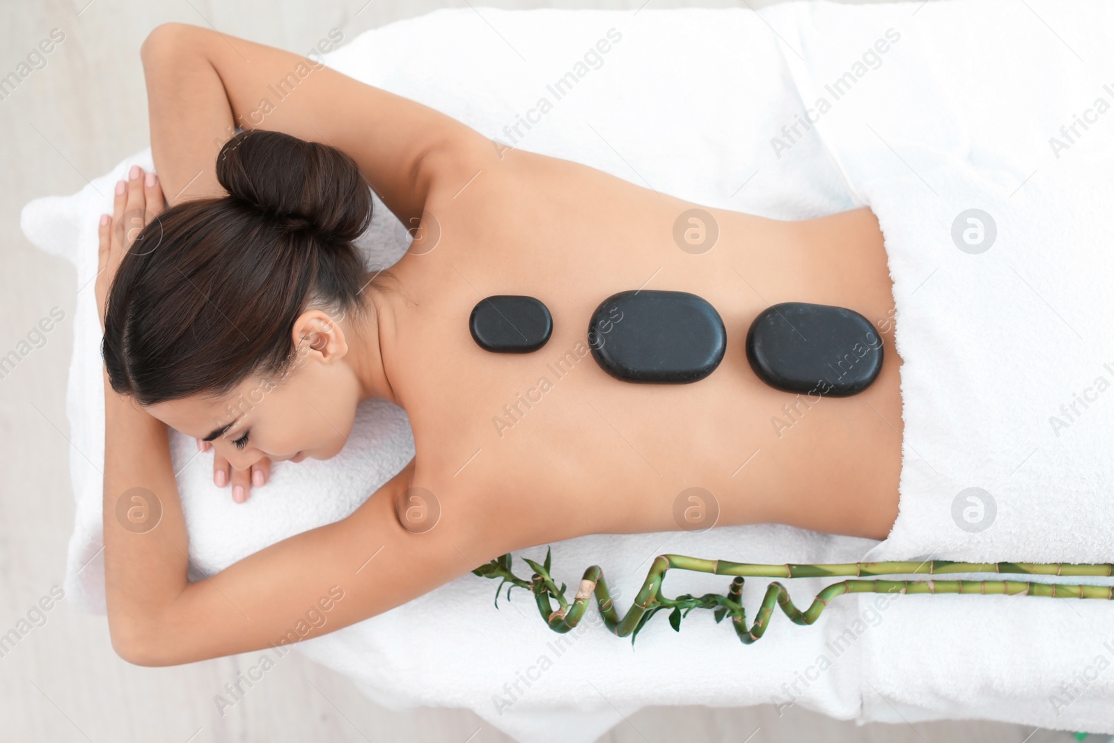 Photo of Beautiful young woman getting hot stone massage in spa salon, top view