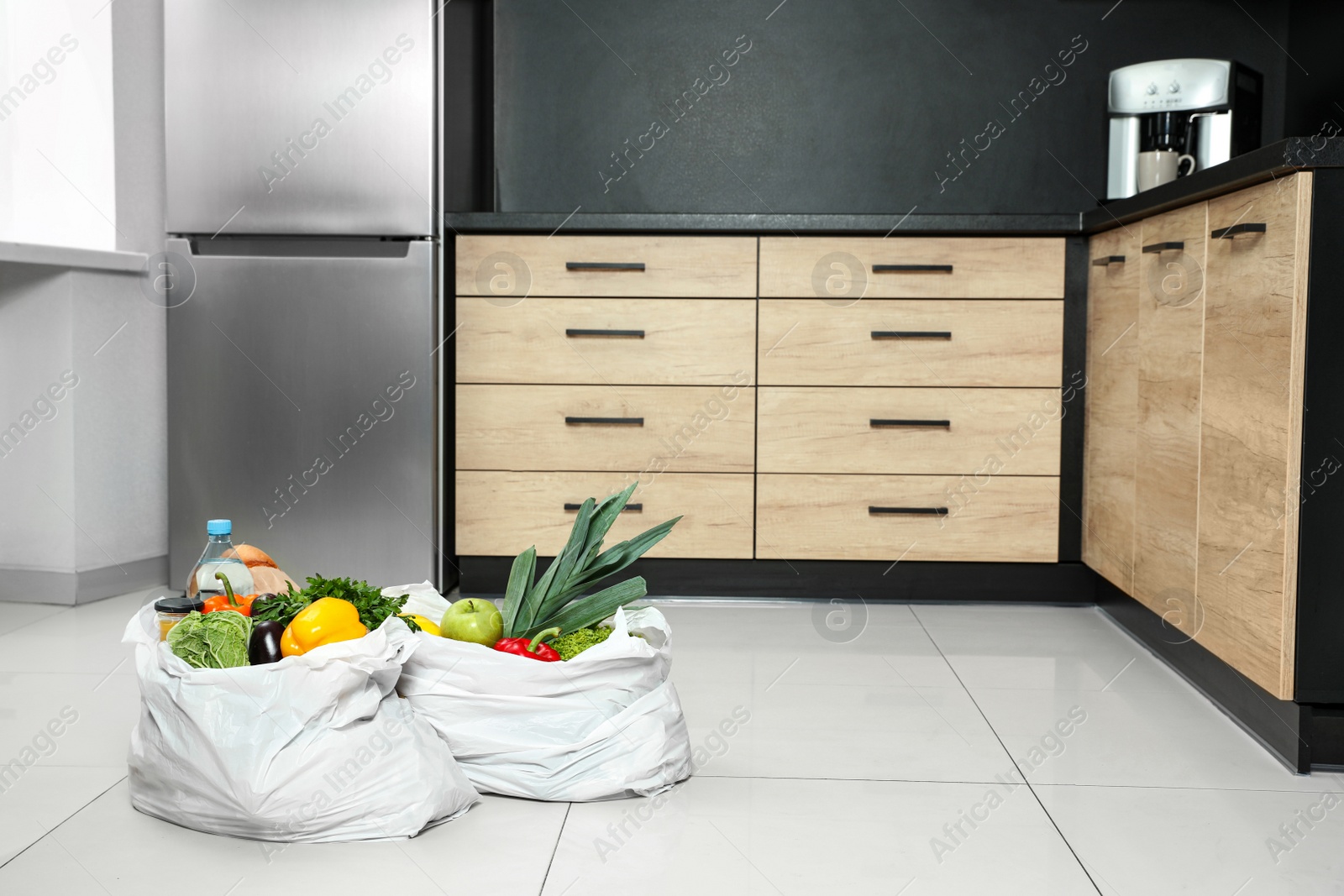 Photo of Plastic bags with vegetables and other products on floor in kitchen. Space for text