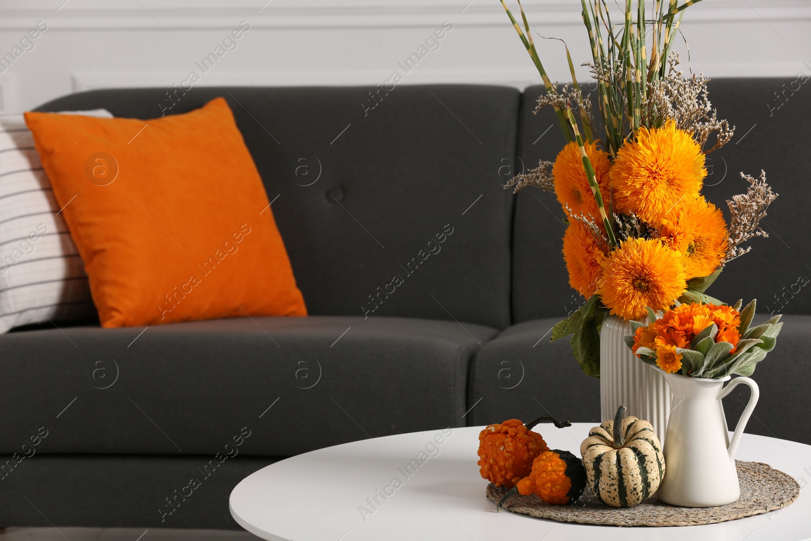 Photo of Beautiful autumn bouquets and pumpkins on coffee table near sofa in room