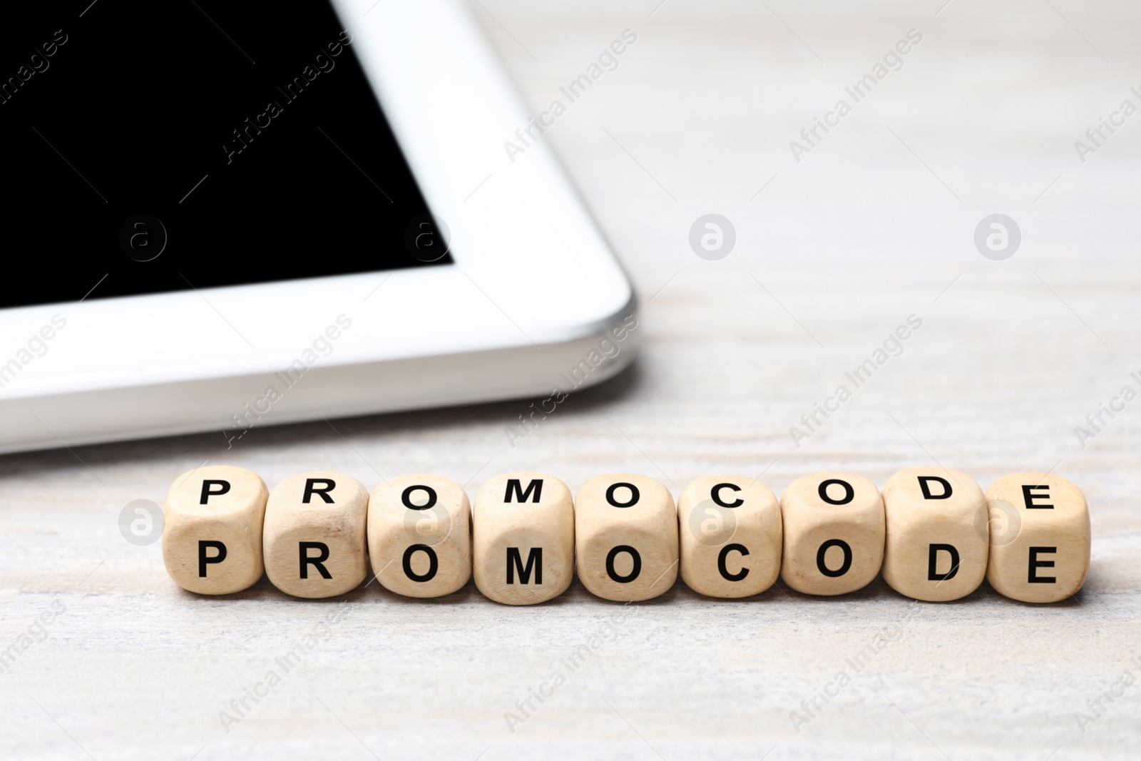 Photo of Word Promocode made of cubes with letters and tablet on white table