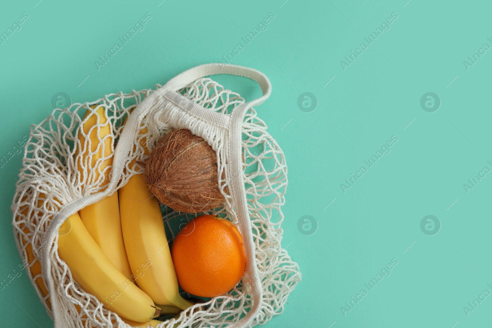 Photo of Net bag with fruits on turquoise background, top view. Space for text