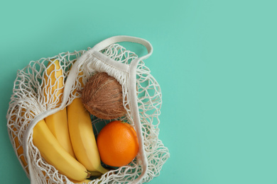 Photo of Net bag with fruits on turquoise background, top view. Space for text