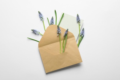 Envelope with beautiful spring muscari flowers and card on light background, top view