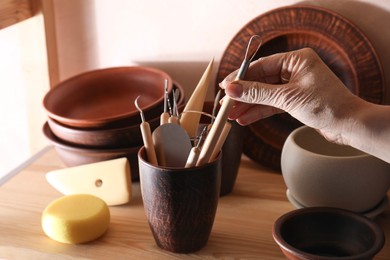 Photo of Woman taking clay crafting tool from cup in workshop, closeup