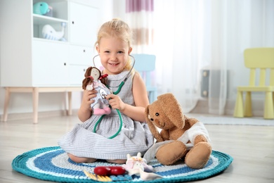 Cute child imagining herself as doctor while playing with stethoscope and toy at home