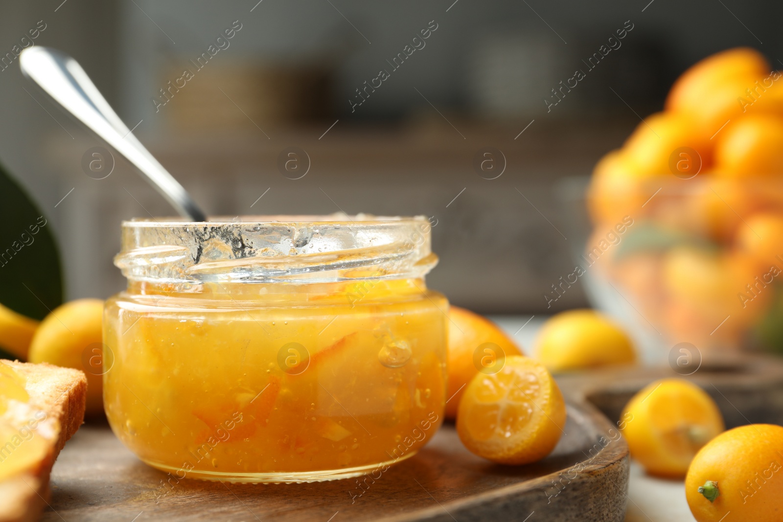 Photo of Delicious kumquat jam in jar and fresh fruits on wooden board, closeup. Space for text