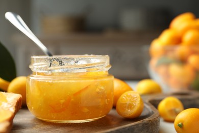 Delicious kumquat jam in jar and fresh fruits on wooden board, closeup. Space for text