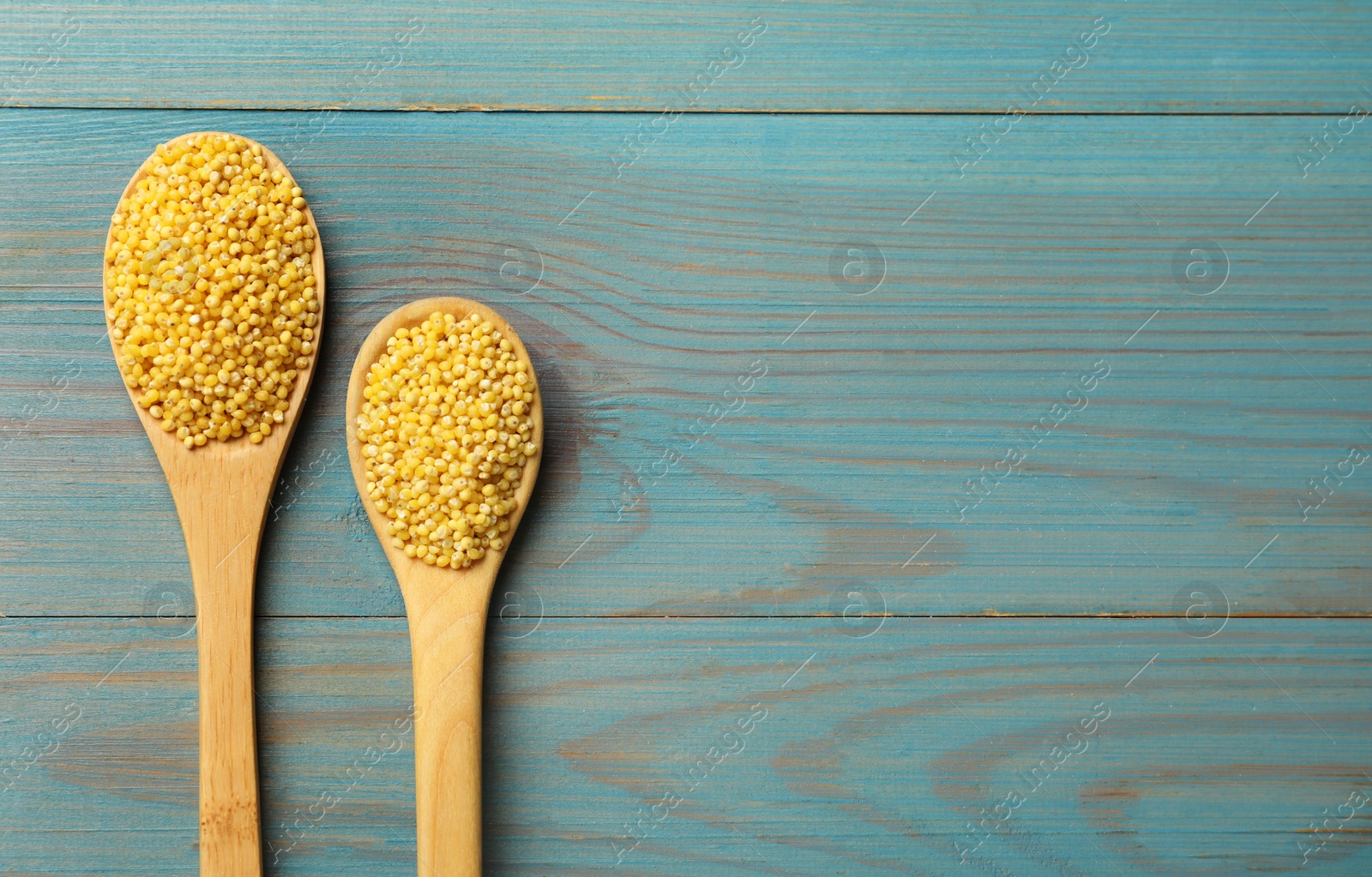 Photo of Spoons with millet groats on light blue wooden table, flat lay. Space for text