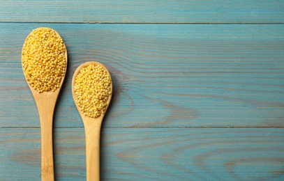 Photo of Spoons with millet groats on light blue wooden table, flat lay. Space for text