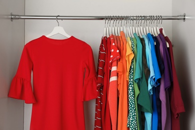 Photo of Hangers with different colorful clothes on rack in wardrobe