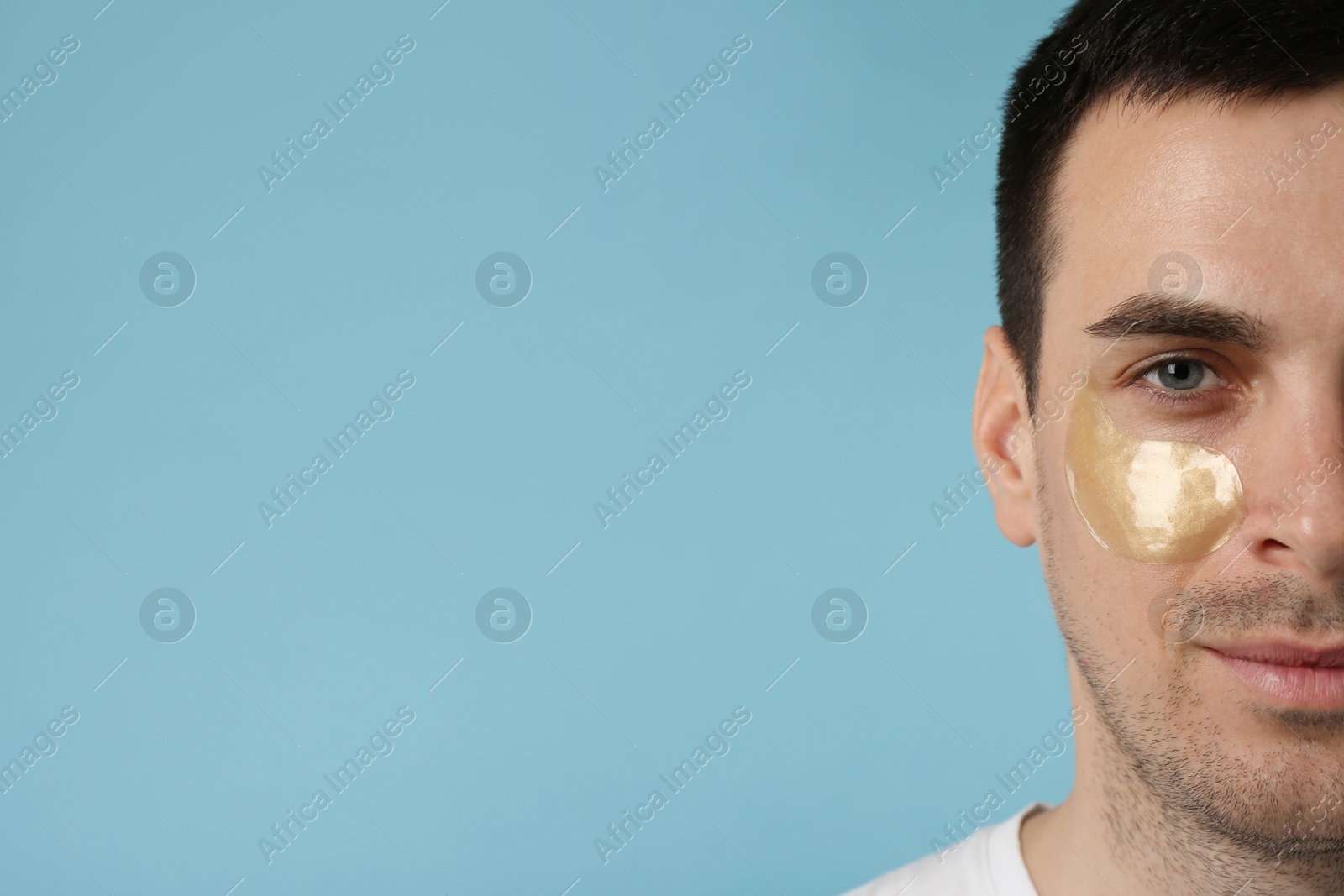 Photo of Young man with under eye patch on light blue background, closeup. Space for text