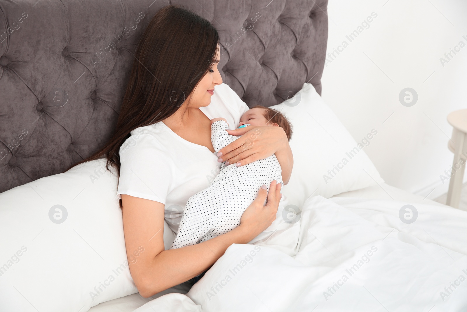 Photo of Happy woman holding her sleeping baby on bed