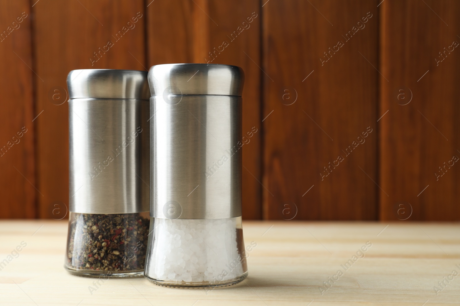 Photo of Salt and pepper shakers on light wooden table, closeup. Space for text