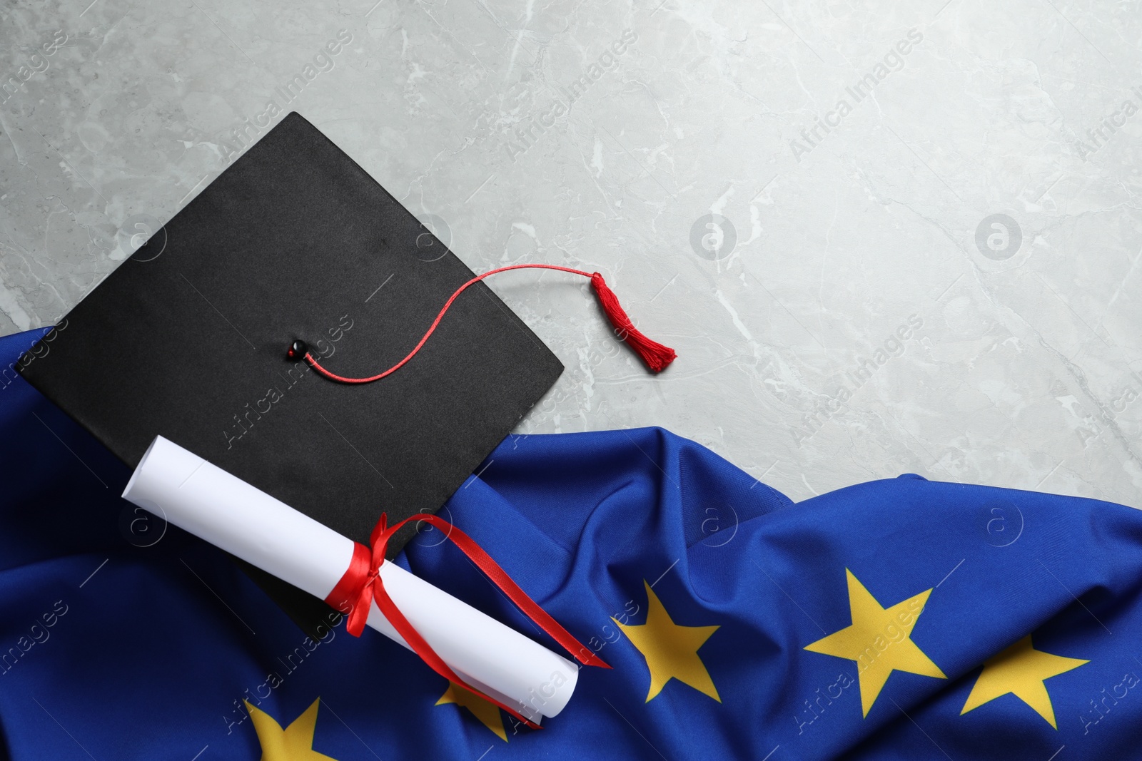 Photo of Black graduation cap, diploma and flag of European Union on light grey marble table, flat lay. Space for text