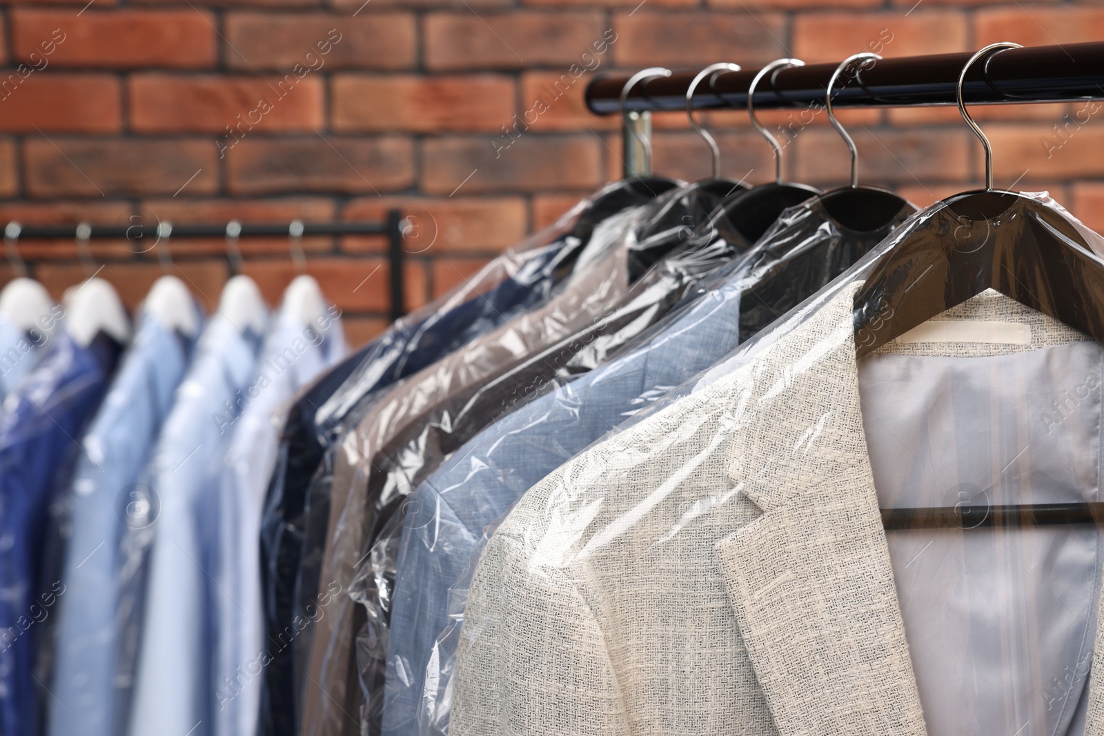 Photo of Dry-cleaning service. Many different clothes hanging on rack against brick wall, closeup