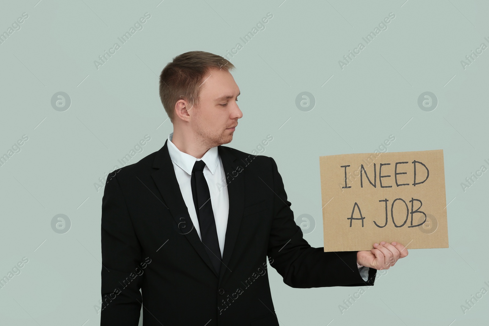 Photo of Unemployed man holding sign with phrase I Need A Job on light grey background