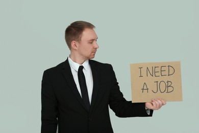 Unemployed man holding sign with phrase I Need A Job on light grey background