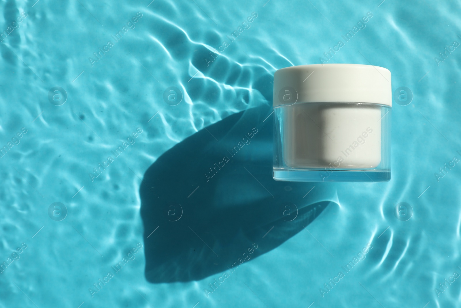 Photo of Jar with moisturizing cream in water on light blue background, top view. Space for text