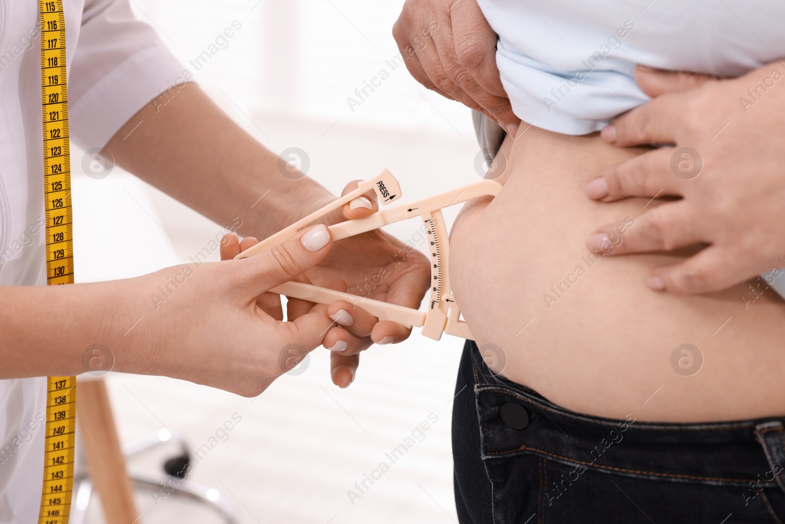 Photo of Nutritionist measuring overweight woman's body fat layer with caliper in clinic, closeup