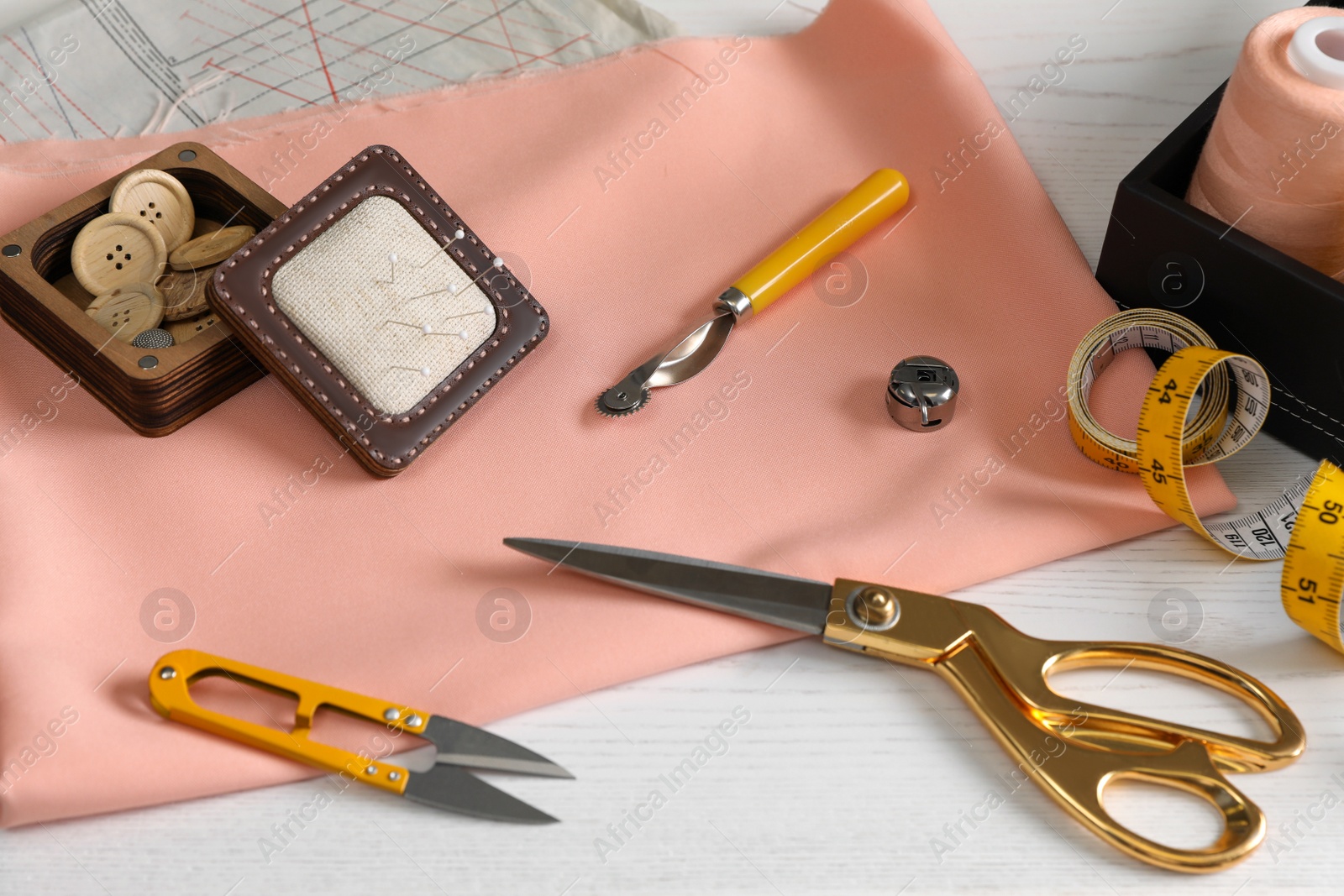 Photo of Set of sewing supplies and accessories with fabric on white wooden table