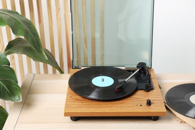 Photo of Stylish turntable with vinyl disc on light wooden table indoors