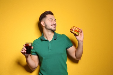 Handsome man with tasty burger and cola on color background