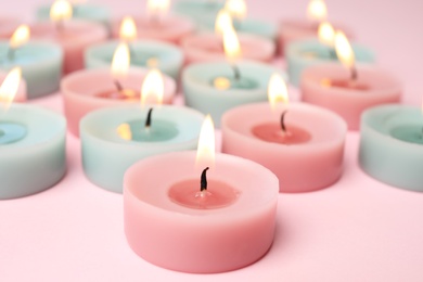 Burning colorful decorative candles on pink background, space for text