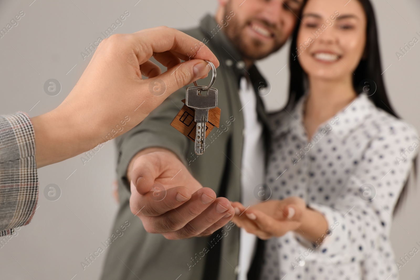 Photo of Real estate agent giving key to happy young couple against grey background, closeup