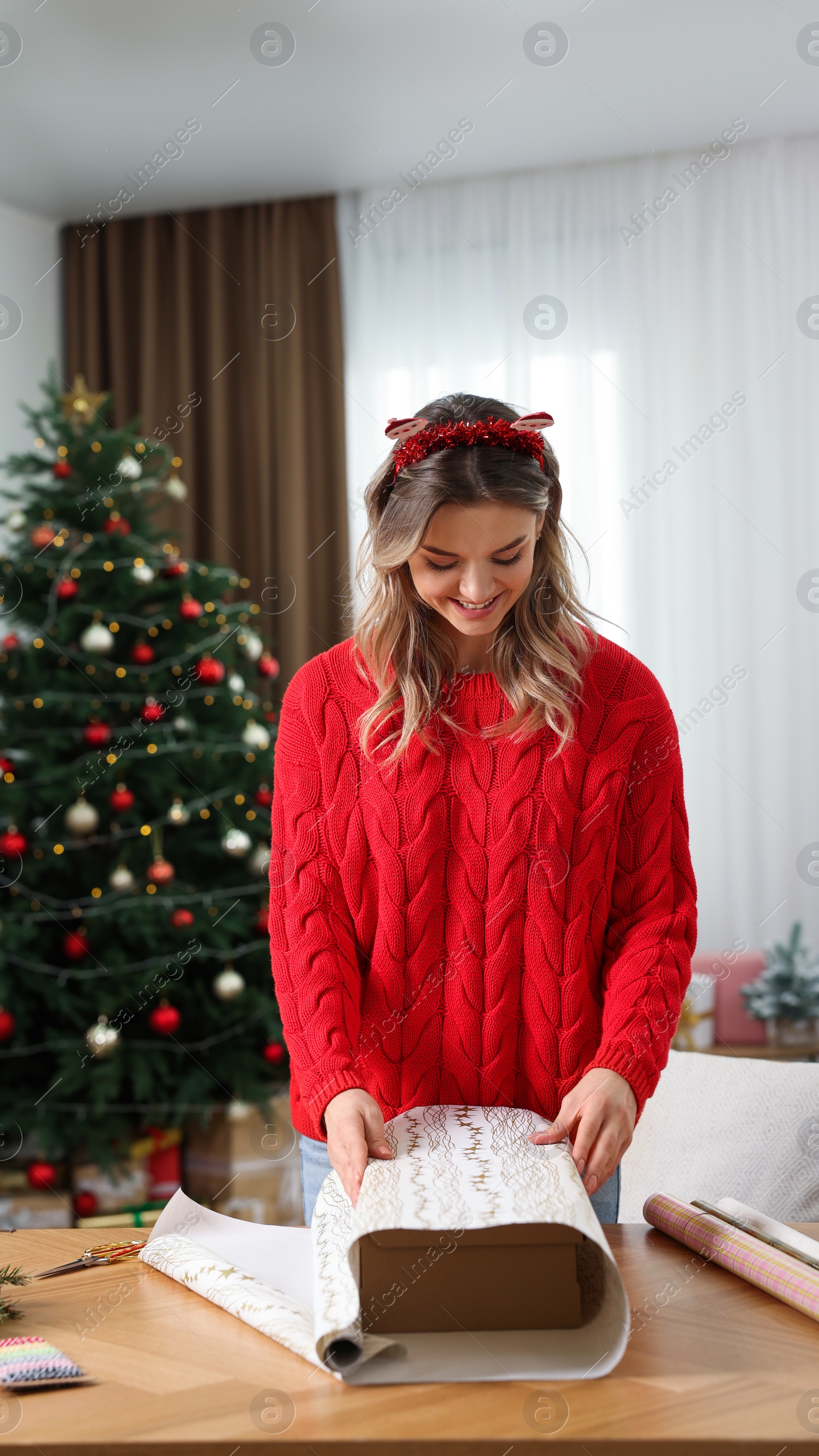 Photo of Beautiful young woman wrapping Christmas gift at home