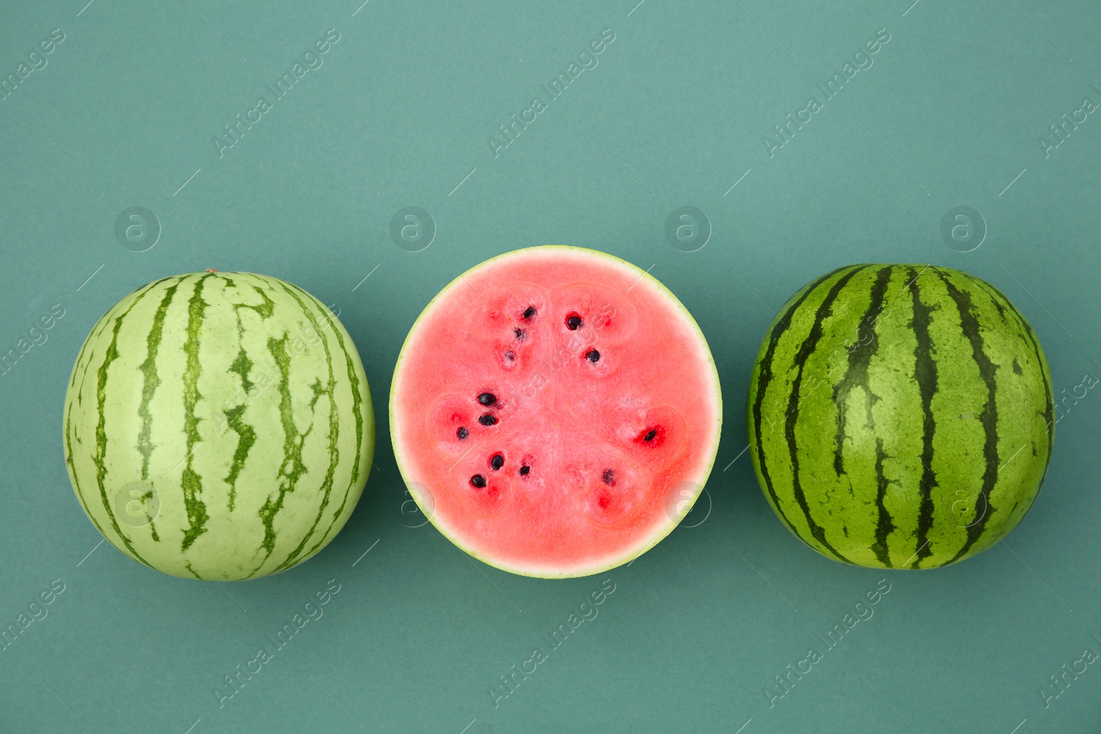 Photo of Cut and whole ripe watermelons on teal background, flat lay