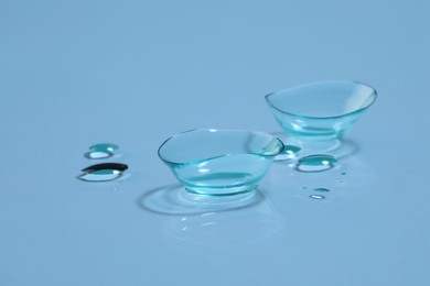 Photo of Contact lenses and drops of water on light blue background