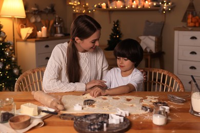 Photo of Mother with her cute little son making Christmas cookies in kitchen