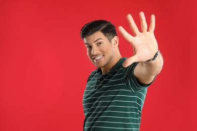 Man showing number five with his hand on red background